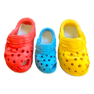 Three chewable rubber shoes for dogs that look like Crocs in red, blue and yellow.